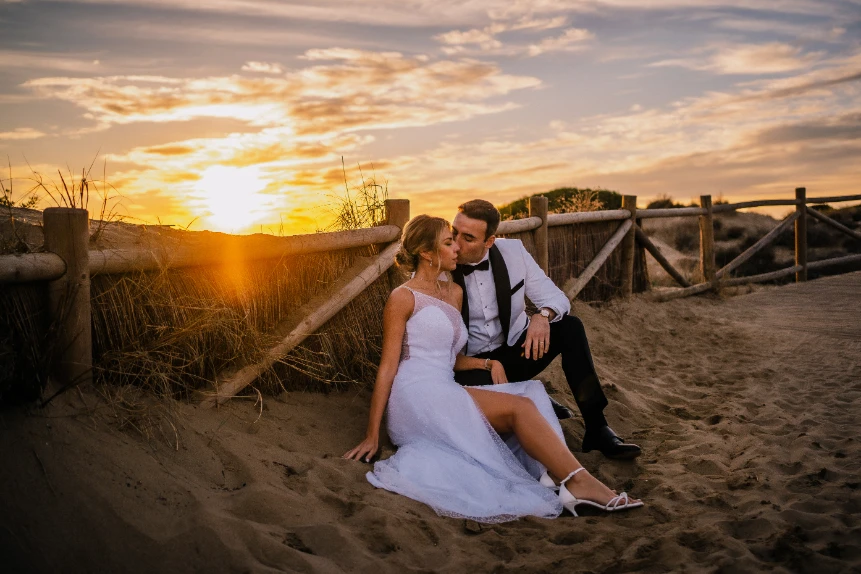 Katerina y Marco en su postboda en playa de Cabopino, con atardecer de fondo.